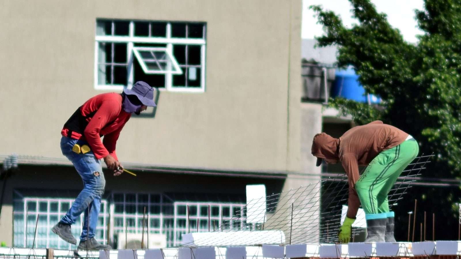 Dois trabalhadores montam a armação da laje de uma casa, em bairro residencial