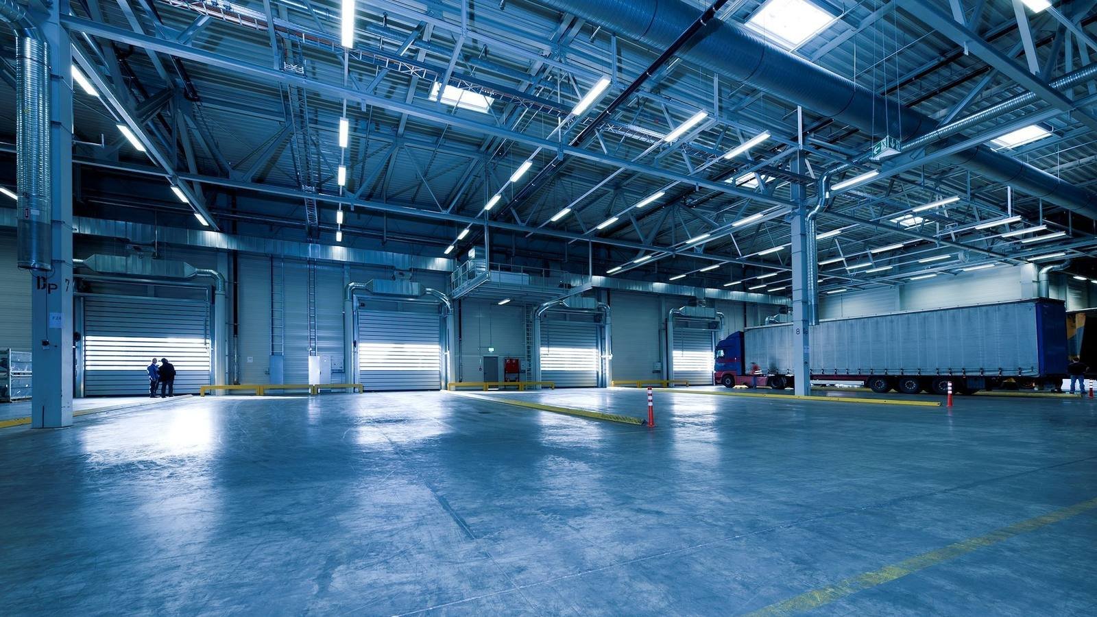Interior de um galpão logístico de empresa, com portas de doca e uma carreta encostada para carregamento